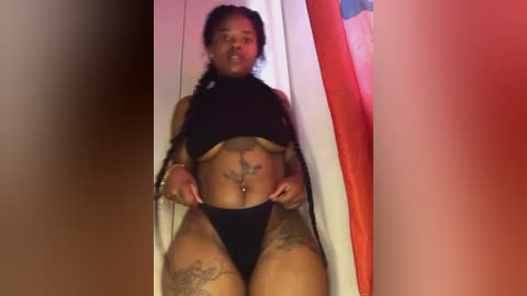 Media: Video of a plus-sized Black woman with tattoos, wearing black lingerie, sitting on a red and white striped chair. She has a confident expression, with a full figure and visible tattoos on her thighs and stomach.