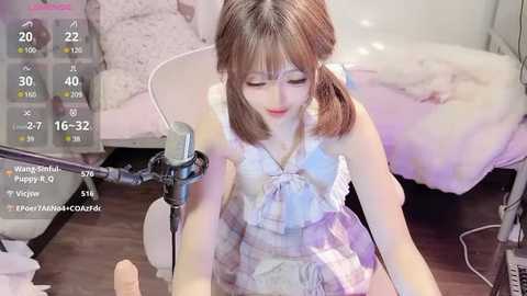 Media: Video of an Asian woman with light skin and straight brown hair in pigtails, wearing a white lace dress, sitting on a wooden floor, holding a microphone, in a cozy bedroom with a bed and a TV screen displaying chatroom messages.