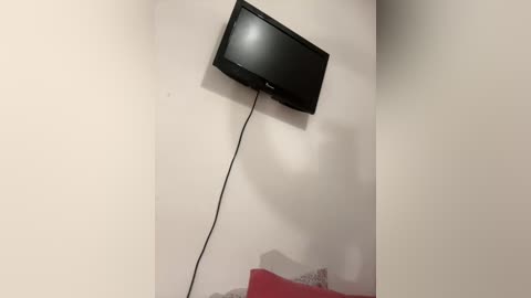 Media: A video of a black flat-screen TV mounted on a beige wall, with a black power cord hanging down. The image shows a simple, minimalist setup with no visible decor or furniture.