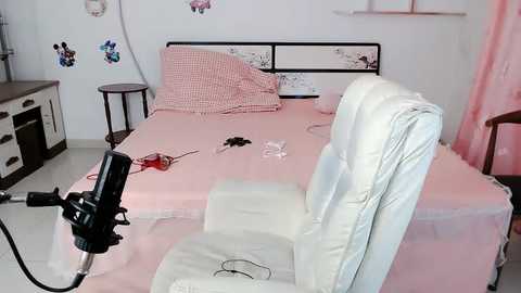 Media: Video of a minimalist, pink-tiled bedroom with a white leather chair, a black microphone, and a neatly made bed with a red pillow.