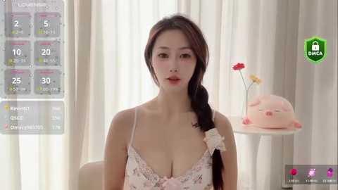 Media: Video of an East Asian woman with fair skin, long black hair, and full lips, wearing a pink lace bra, standing in a bright, minimalist room with soft curtains and a green \"BANG\" logo.