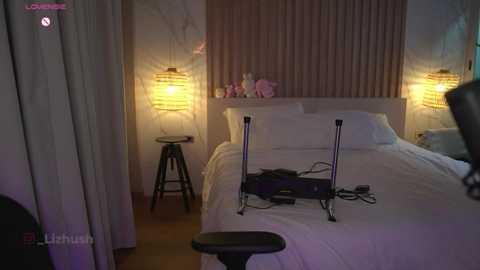 Media: Video of a dimly lit, modern hotel room with a white bed, two bedside lamps, a stool, and a laptop on the bed.