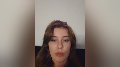 Media: Video of a Caucasian woman with long, wavy brown hair and fair skin, wearing minimal makeup, blowing a kiss towards the camera against a plain, off-white background.