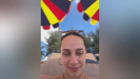 Media: A video of a smiling woman with fair skin, dark hair pulled back, wearing a beige dress, standing outdoors against a blue sky with a German flag in the background.