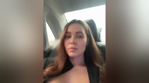 Media: A blurred video of a young woman with long, brown hair, wearing a black top, sitting in a car. The background shows the car's interior and outside light.