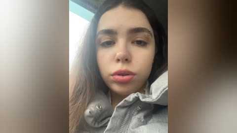 Media: Video of a young Latina woman with straight, dark brown hair, wearing a gray hoodie, and a slight frown. Her skin tone is light brown, and she has a neutral expression.