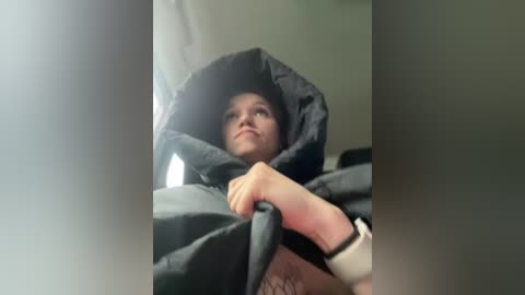 Media: Video of a young boy, with light skin and dark hair, bundled in a black winter coat, looking upwards, possibly in a car, with blurred background.