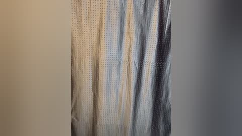 Media: Video of a textured, perforated shower curtain with vertical stripes in shades of white, gray, and blue, hanging against a plain beige wall. The curtain's fabric appears slightly wrinkled, giving it a soft, lived-in look.