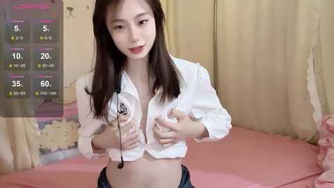 Media: A video of a young Asian woman with long brown hair, wearing a white, unbuttoned blouse, and a headset, in a pink bedroom.