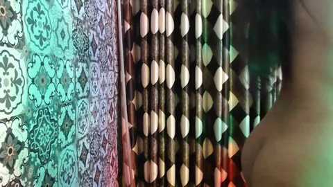 Media: Video of intricate, multicolored fabric patterns featuring geometric designs in shades of green, turquoise, brown, and beige. The textures are rich and detailed, with the fabric appearing woven or embroidered.