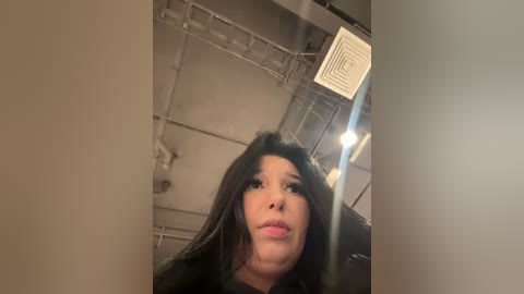 Media: A video of a woman with long, dark hair and a neutral expression, captured from behind a partially closed door in a dimly lit, industrial setting.