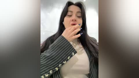 Media: A video of a woman with long dark hair, wearing a pinstriped blazer, holding a phone to her ear, with a blurred background.