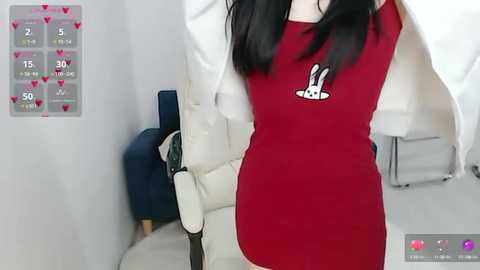 Media: Video of a woman with long black hair, wearing a red dress with a white apron, holding a broom in a white room.