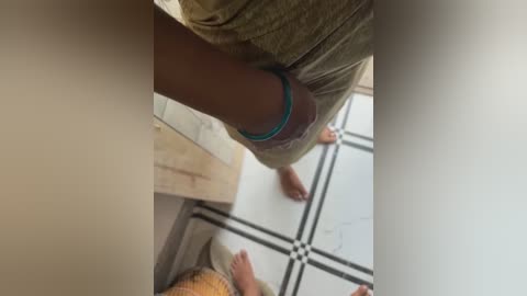 Media: A video captures a person's lower body in beige shorts, walking in a tiled bathroom with white and black geometric patterned floor.