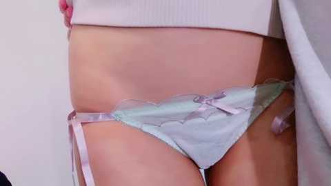 Media: Video of a light-skinned person's torso, wearing pastel blue lace panties with a pink bow. The person is lifting a white top, revealing their flat stomach and toned abs.