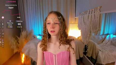 Media: A video of a young girl with curly brown hair, wearing a pink corset, in a cozy, dimly lit bedroom with fairy lights and bohemian decor.