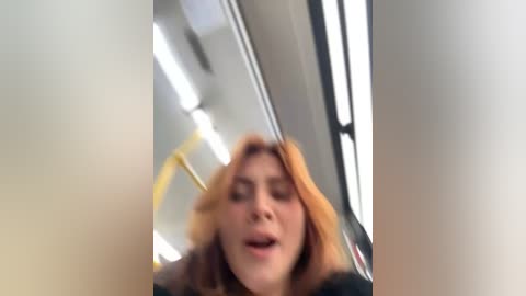 Media: A blurry video of a young woman with light brown hair, eyes closed, mouth slightly open, in a dimly lit, modern subway car with bright fluorescent lights and reflective surfaces.