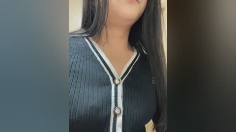 Media: Video of a woman with long, straight black hair, wearing a black, ribbed cardigan with white buttons and trim, against a blurred background.