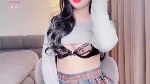 Media: Video of an Asian woman with long black hair, wearing a sheer black lace bra and a plaid skirt, posing indoors by a couch.