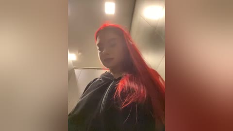 Media: Video of a young woman with vibrant red hair, wearing a dark hoodie, walking down a dimly lit hallway with soft, ambient lighting.