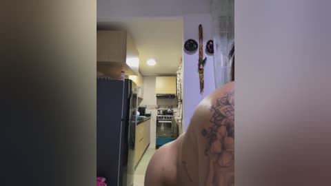 Media: Video of a person with a tattoo on their shoulder standing in a narrow hallway, with a kitchen visible in the background.