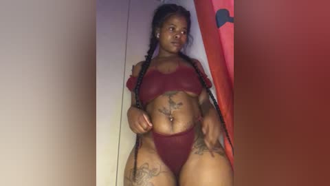 Media: A video of a plus-sized Black woman with braided hair, wearing red lingerie, sitting on a red couch against a white wall, showing off tattoos.