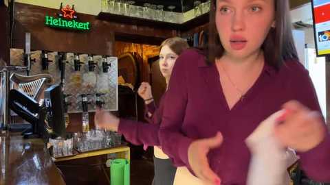 Media: Video of two young women in a pub, one in a maroon sweater, the other in a red shirt, with a bar backdrop featuring Heineken signage and glassware.