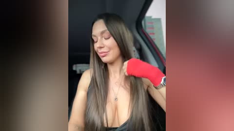 Media: Video of a Latina woman with long, straight brown hair, wearing a black tank top, red wristband, and a necklace. She's adjusting her hair in a dimly lit room, with a blurred background.