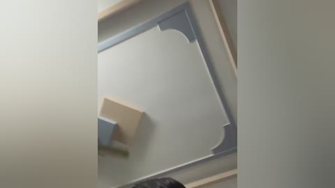 Media: Video of a modern, minimalist room with a large, light grey, geometrically shaped mirror mounted on the wall. The mirror has blue and beige accents.