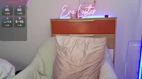 Media: A video of a cozy bedroom with a pink pillow, wooden headboard, Eva Aster neon sign, and a digital clock showing 4:59 AM.