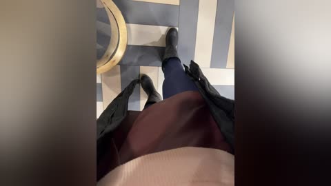 Media: Video of a person's legs, wearing dark blue tights, black shoes, and a maroon skirt, walking down a tiled hallway with grey and beige circular pattern.