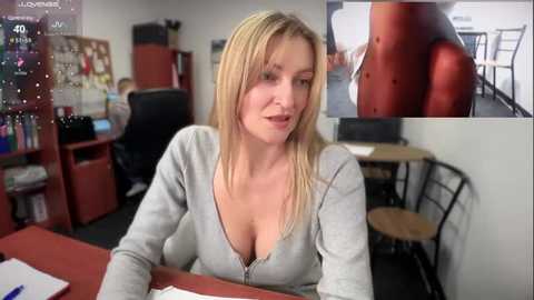 Media: Video of a blonde Caucasian woman in a gray hoodie, seated at a desk in an office, with a large red office chair behind her.