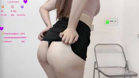 Media: A video of a woman with light skin and long brown hair, wearing a pink bra and black skirt, lifting her skirt to reveal her bare buttocks.