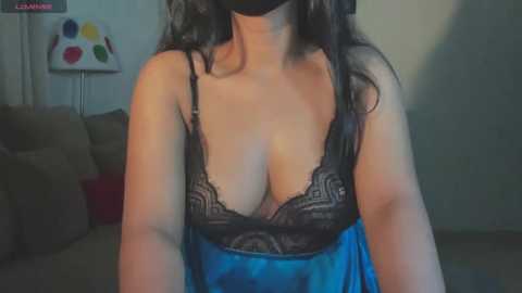 Media: A video of a woman in a blue satin robe with black lace trim, showing ample cleavage, taken in a dimly lit living room.