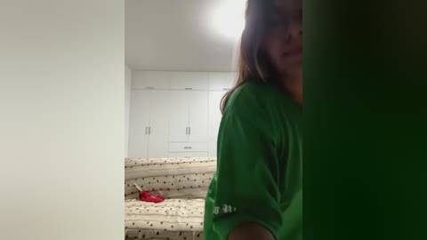 Media: A video shows a woman in a green shirt peering through a doorway, with a beige-patterned sofa and white cabinets in a dimly lit room in the background.