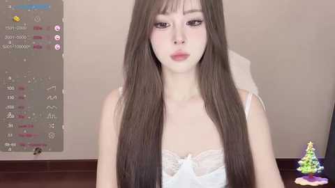 Media: Video of a young Asian woman with long brown hair and fair skin, wearing a white lace bra, in a neutral indoor setting.