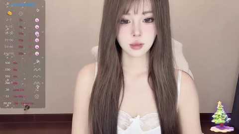 Media: Video of a fair-skinned Asian woman with long, straight brown hair, wearing a white lace bralette, against a beige wall, with a virtual calendar and colorful toys in the background.