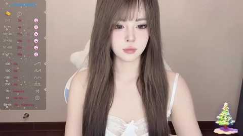 Media: Video of a young Asian woman with long, straight brown hair, wearing a white lace bra, indoors, with a calendar and a small Christmas tree in the background.