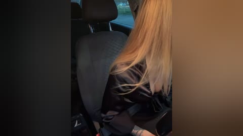 Media: A video showing a blonde woman in a black leather jacket, seated in a car with dim lighting, looking away.