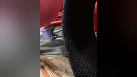 Media: A close-up video showing a person's torso with a red shirt, blue jeans, and a black, textured backpack, captured in a dimly lit room.