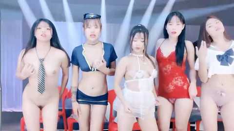 Media: Video of five Asian women in provocative lingerie and costumes posing in a modern room with white walls and red chairs.