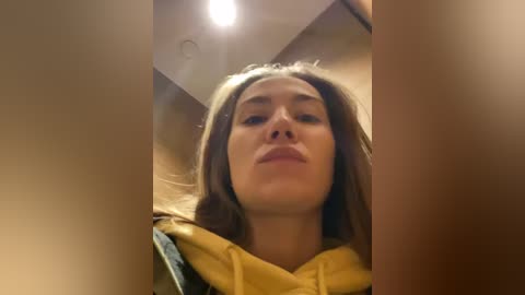 Media: A video of a young woman with light brown skin, long brown hair, and a yellow scarf, looking slightly downwards, taken indoors under dim lighting.