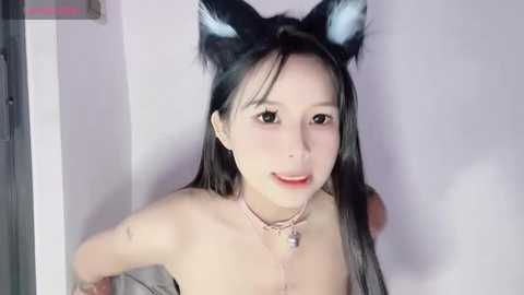 Media: Video of an East Asian woman with long black hair, wearing black cat ears and a pink choker. She has a light skin tone, and is smiling with a slightly open mouth.