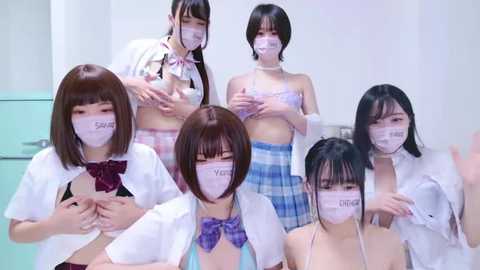 Media: Video of six Asian women in school uniforms with white masks, standing in a sterile room, some with their shirts open revealing cleavage.