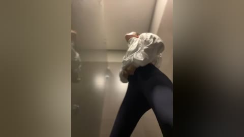 Media: Video of a person in a white shirt and black leggings, captured from a low angle, creating a distorted, blurry reflection on a glass wall.