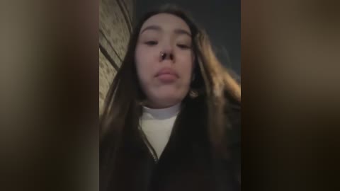 Media: A blurry video of a young woman with long brown hair, wearing a white shirt, standing against a brick wall.