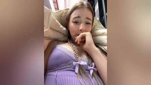 Media: A video of a young Caucasian woman with long, straight blonde hair and fair skin, lying on her side in bed, wearing a purple ribbed nightgown with a lace trim and a small bow.