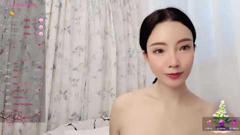 Media: Video of an Asian woman with fair skin, straight black hair, and a slender physique, topless, in a bedroom with floral-patterned curtains and a pink and white decor.