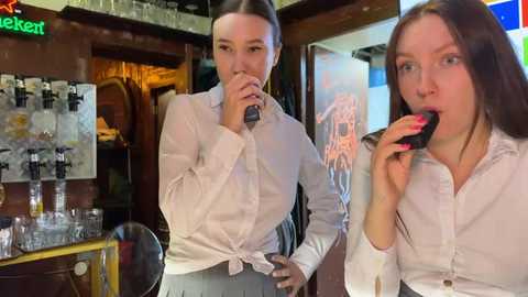 Media: Video of two young women, one with a microphone, the other eating a cookie, in a cozy, dimly-lit bar setting with a beer tap and decorative lights.