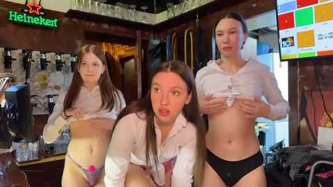 Media: Video of three young women in a bar, lifting white shirts to reveal black panties, Heineken sign visible.